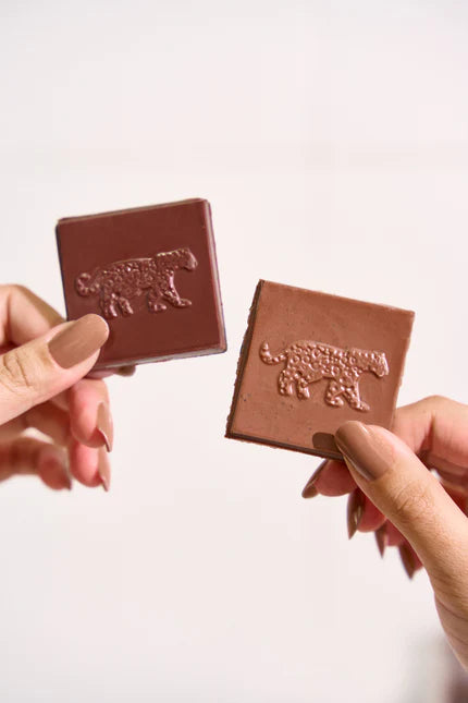 Two hands holding up two Karu chocolate bars with a visible brand logo against a white background