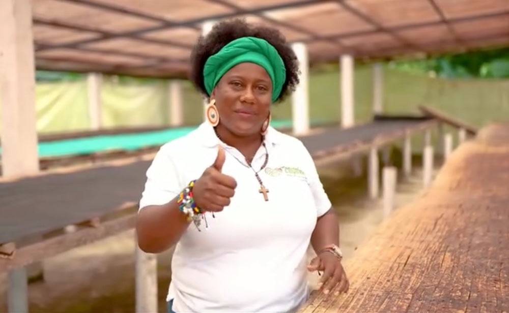 Person wearing a white shirt with a Corpoteva logo, giving a thumbs-up gesture in an outdoor setting.